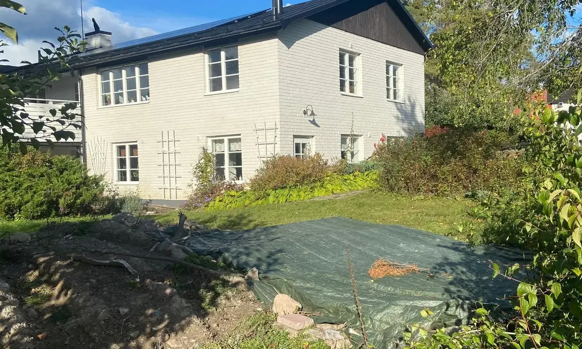 Vitt hus med mörk tak och trädgård. En presenning täcker en del av trädgården, kanske ett gömt hus skatt?