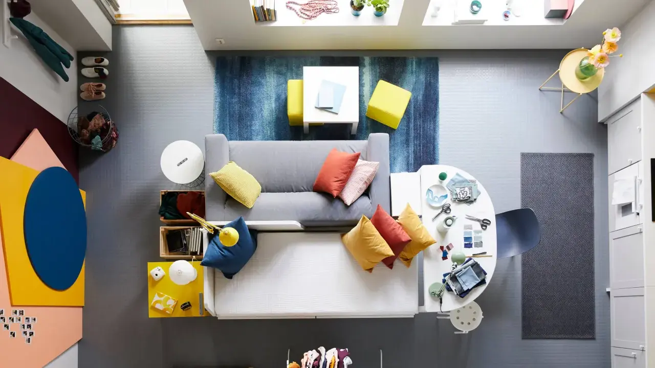 Ett litet vardagsrum med matplats, fyllt med färg och kreativitet. En grå soffa med kuddar i orange och gult, en vit matplats med stolar och en blå matta.