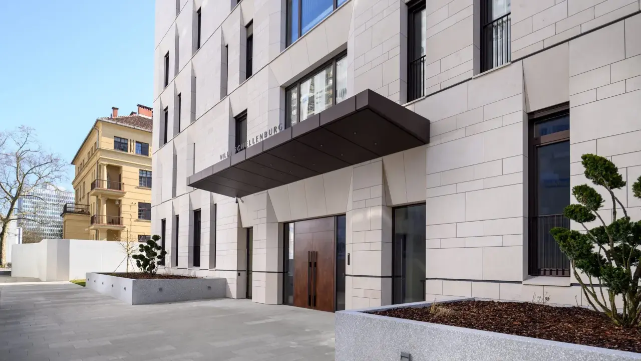 Modern villa med stenfasad och dubbeldörrar. En skylt visar "VILLA SCHELLENBURG". Kanske en symbol för en brf konkurs?
