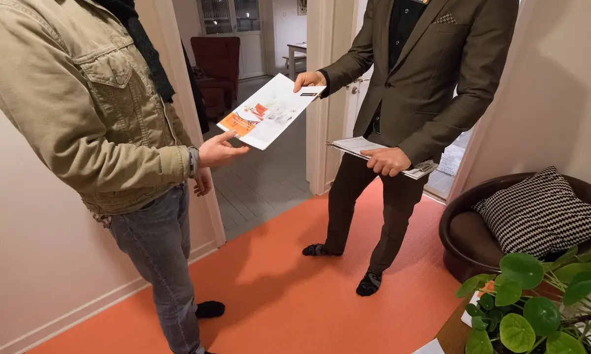En mäklare ger en broschyr om bostäder till en kund. Kanske handlar det om en kontantinsats på 5 procent.