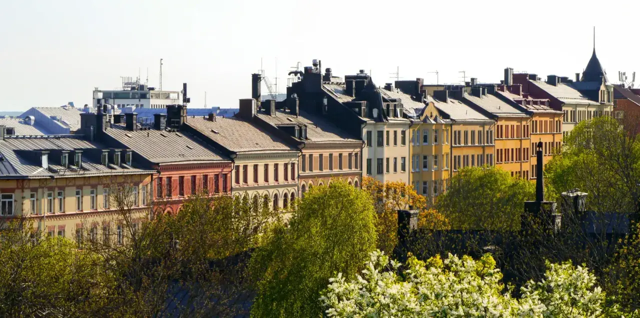 Färgglada husfasader i stadsmiljö, med träd i förgrunden. En vy som kan ge en känsla av belåning per kvadratmeter i en levande stad.