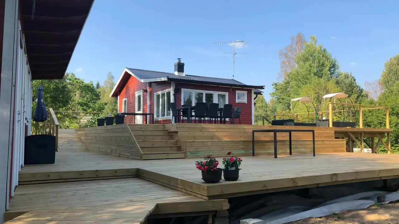 Stor altan i trä med trappor och sittplatser framför ett rött hus. Perfekt altan inspiration för sommarens grillkvällar.
