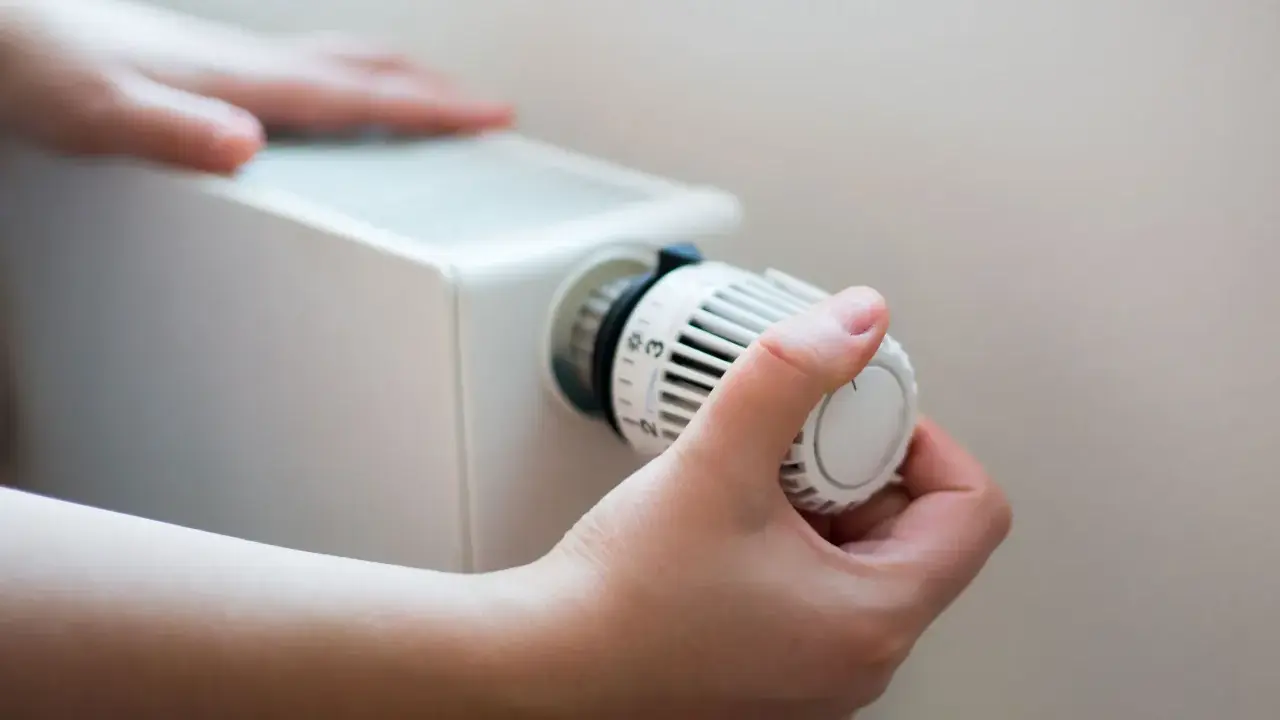 En hand vrider på termostaten till ett vattenburet element för att justera värmen.