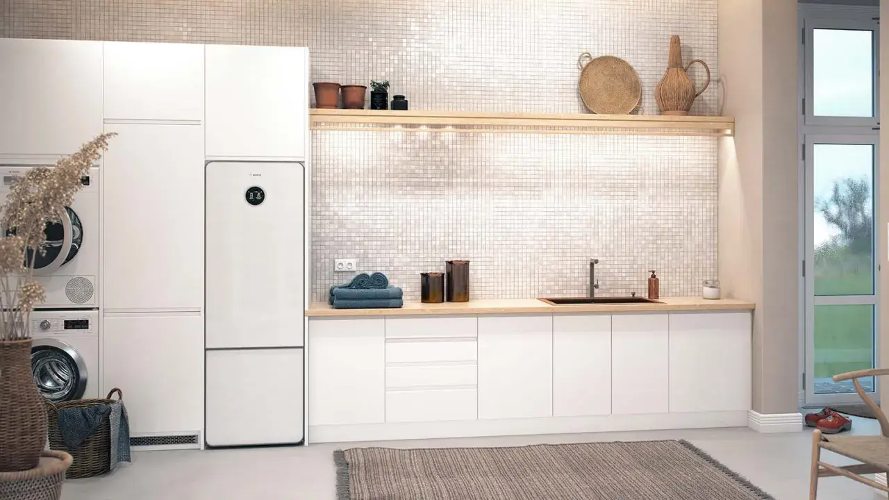 Vit tvättstuga med Bosch Compress 7800i värmepump, tvättmaskin, torktumlare och en bänkskiva med diskho.