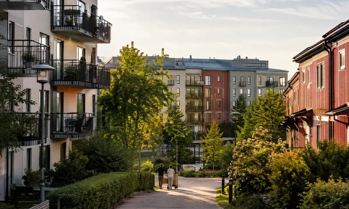 Två personer flyttar kartonger på en gångväg i ett modernt bostadsområde. Kanske redo att hyra ut i andra hand?