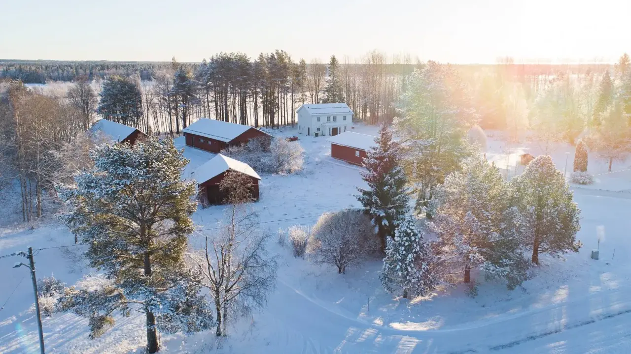 Snötäckt gård med vita och röda byggnader. Solen lyser på ett nybyggt hus, en idyllisk vy som ger tankar om framtida fastighetsavgift.