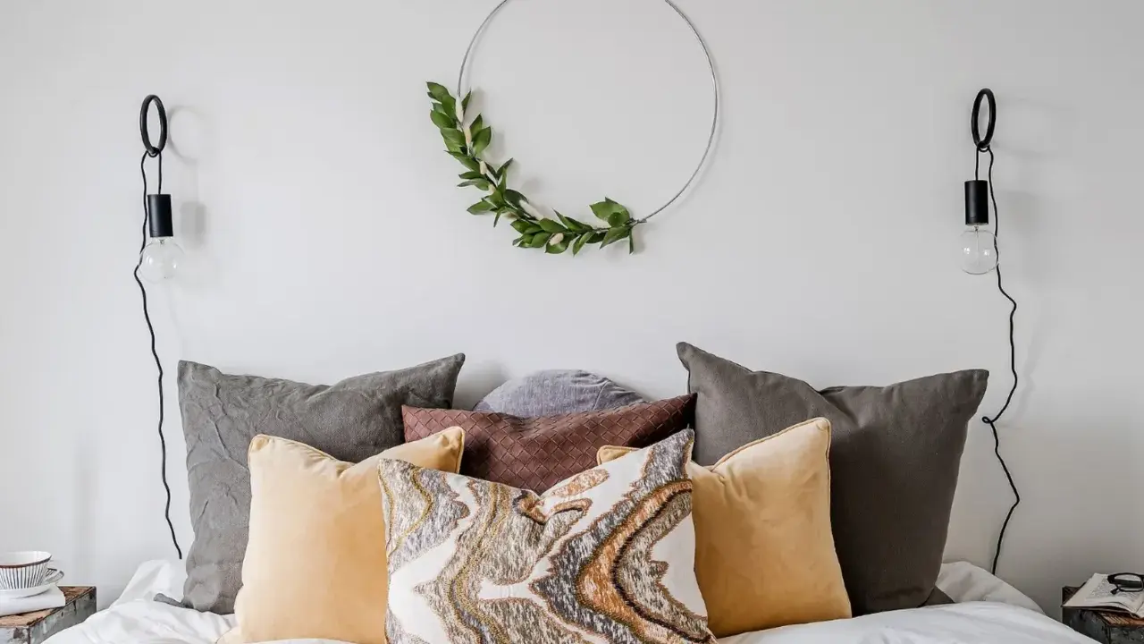 Sovrum inspiration med en säng fylld av kuddar i olika färger och texturer, en grön krans på väggen och minimalistiska vägglampor.
