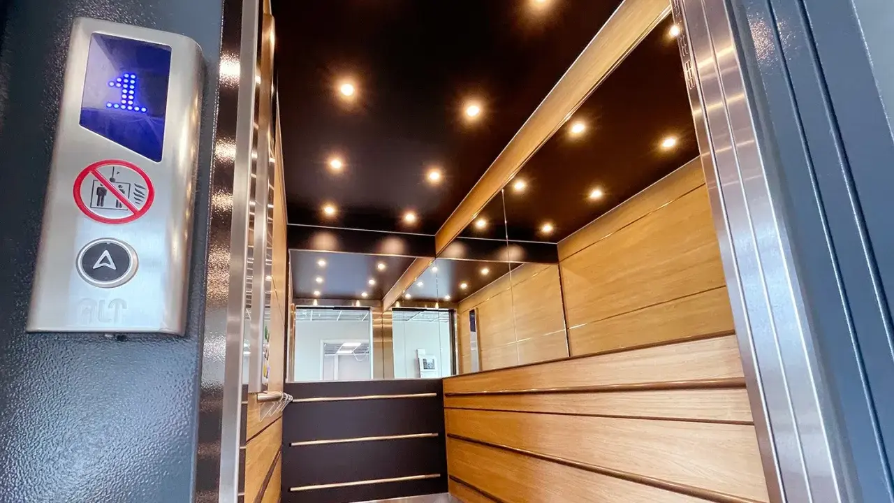Insidan av en modern, men ändå gammal hiss, med träpaneler, speglade väggar och en svart tak med spotlights. En knapp med siffran 1 lyser.