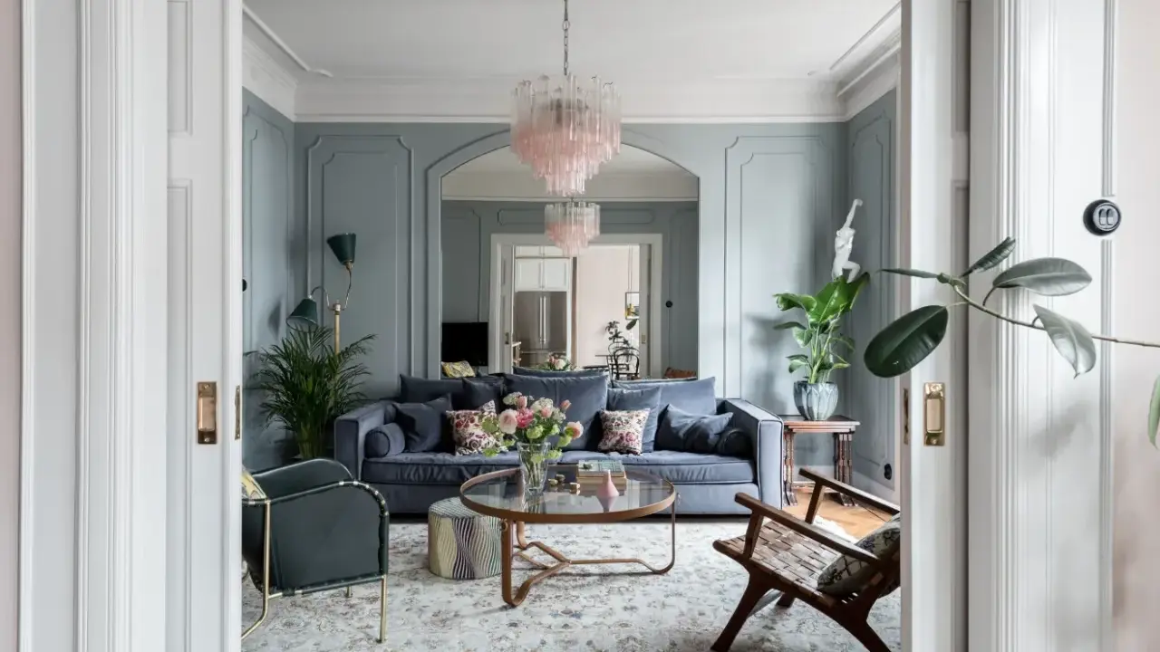 Ett elegant vardagsrum med blåa väggar, en mörkblå soffa, en rosa kristallkrona och en vacker matta. Perfekt vardagsrum inspiration för ett stilfullt hem.