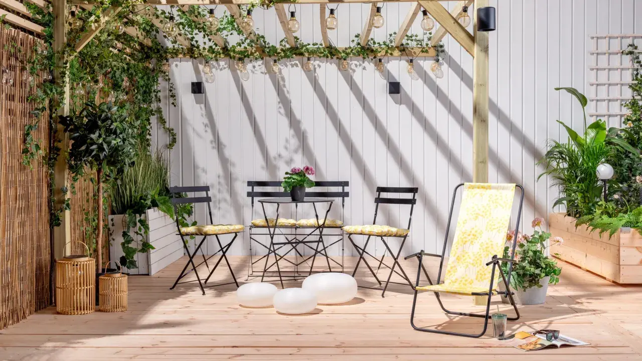 En mysig uteplats med träpergola, belysning och sittgrupp. Buskar insynsskydd ger avskildhet.