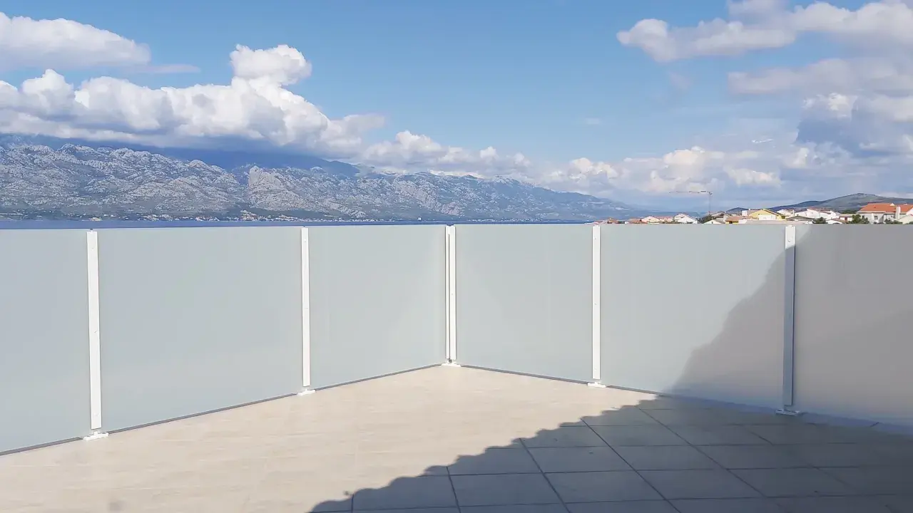 Frosted glass privacy screens on a tiled patio with a view of mountains and the sea.