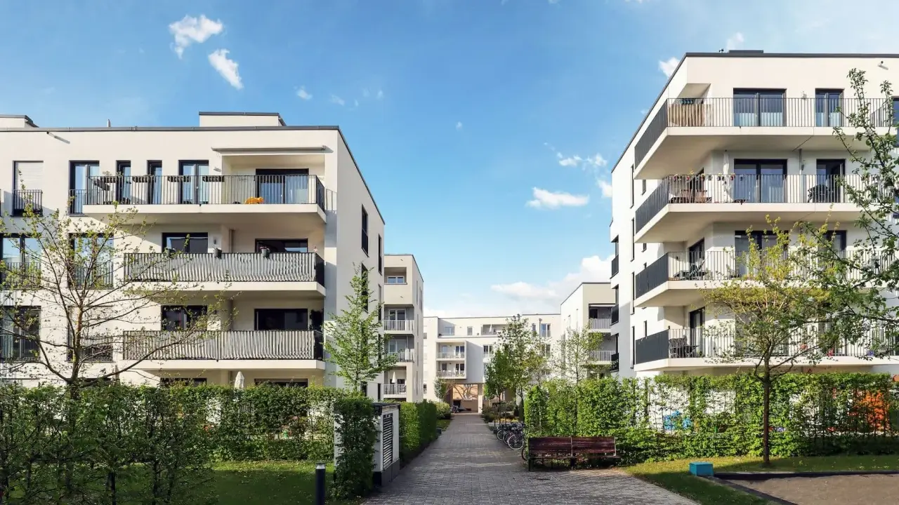 Moderna bostadshus med balkonger och grönska. En lugn innergård med gångväg, bänk och cyklar. Perfekt för en trygg boendemiljö, som en revisor brf skulle uppskatta.
