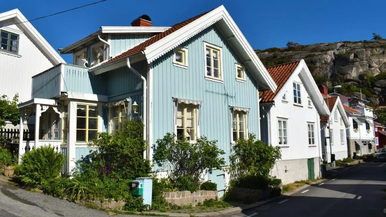 Blå och vita trähus längs en gata, med klippor i bakgrunden. Undrar hur mycket fastighetsskatt dessa vackra hus har.