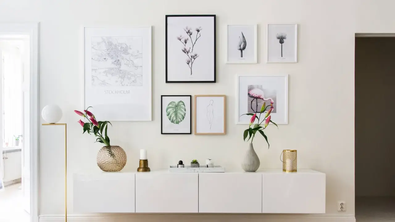Ett modernt, inrett avlastningsbord med konstverk och blommor. En vit skänk med en guldig lampa, vaser och ljus.