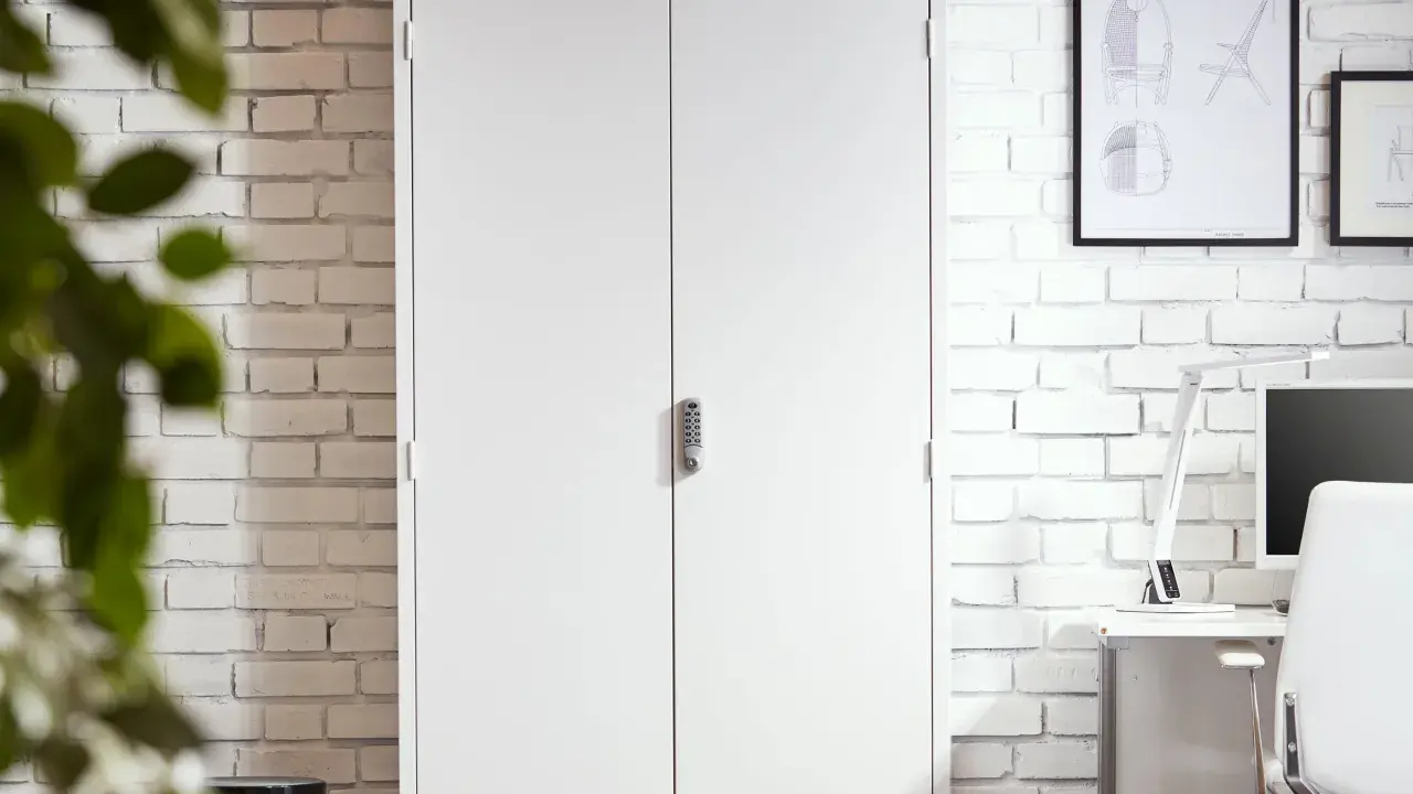 Vita dubbeldörrar med kodlås ger ett tryggt boende. En vit tegelvägg och en grön växt i förgrunden.