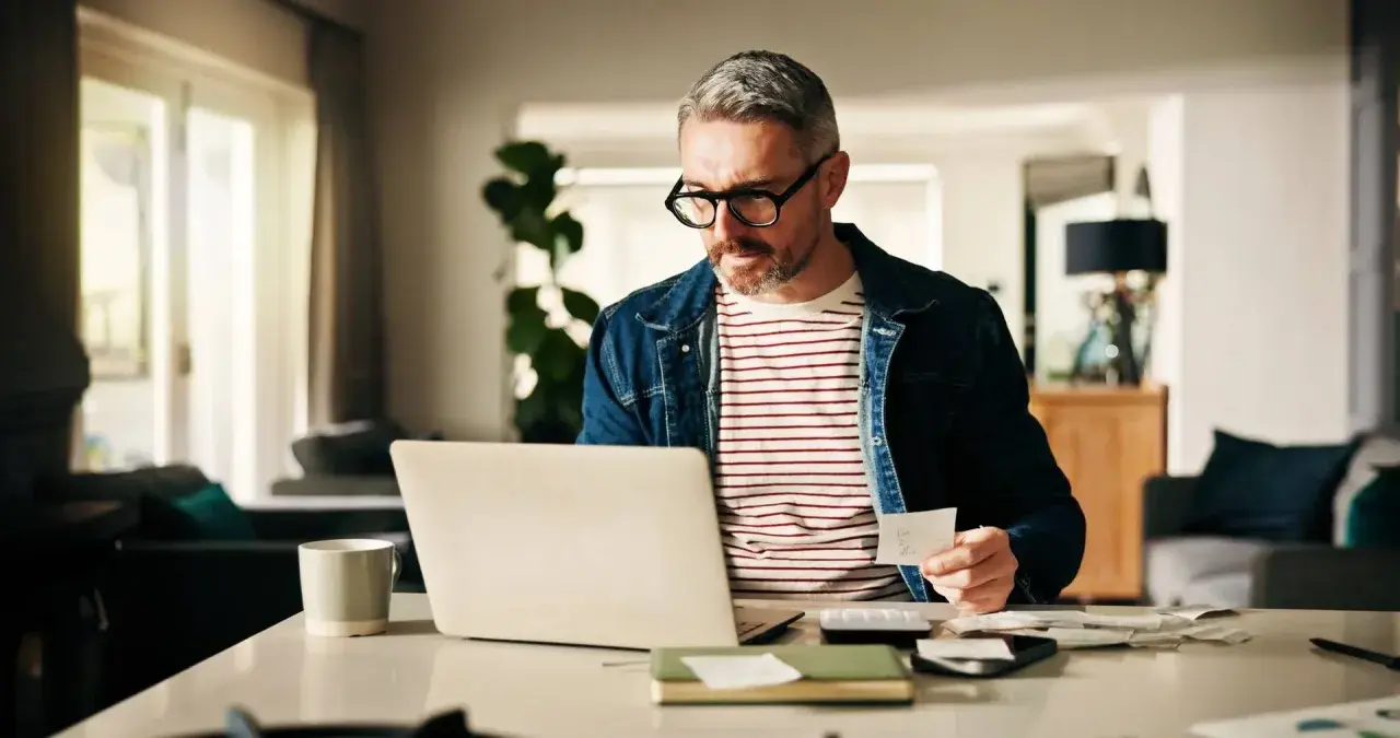 Man med glasögon kollar papper och laptop, kanske för att se vad kollar banken vid bolån.