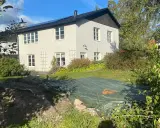 Vitt hus med mörk tak och trädgård. En presenning täcker en del av trädgården, kanske ett gömt hus skatt?