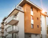 Modernt bostadshus med träfasad och balkonger. Solen skiner, en bild av trygghet och ansvarsfrihet för styrelse.