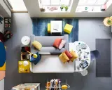 Ett litet vardagsrum med matplats, fyllt med färg och kreativitet. En grå soffa med kuddar i orange och gult, en vit matplats med stolar och en blå matta.