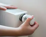 En hand vrider på termostaten till ett vattenburet element för att justera värmen.