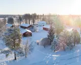 Snötäckt gård med vita och röda byggnader. Solen lyser på ett nybyggt hus, en idyllisk vy som ger tankar om framtida fastighetsavgift.
