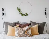 Sovrum inspiration med en säng fylld av kuddar i olika färger och texturer, en grön krans på väggen och minimalistiska vägglampor.