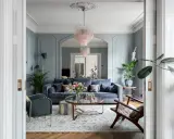 Ett elegant vardagsrum med blåa väggar, en mörkblå soffa, en rosa kristallkrona och en vacker matta. Perfekt vardagsrum inspiration för ett stilfullt hem.