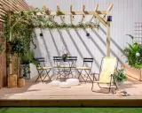 En mysig uteplats med träpergola, belysning och sittgrupp. Buskar insynsskydd ger avskildhet.