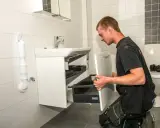 En man knäböjer och hjälper till att montera badrumsskåp bredvid ett handfat och en toalett.
