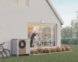 En familj njuter av en solig dag vid sitt hus, med en NIBE S2125-12 värmepump som diskret står vid sidan.