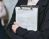 Person håller ett dokument med rubriken "HOME INSURANCE POLICY". Detta kan vara en del av ett hyresavtal lokal.