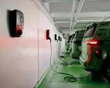 Rad med gröna elbilar laddas vid laddstolpar. Systemet för debitering laddstolpar är igång, vilket syns på de röda lamporna.