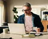 Man med glasögon kollar papper och laptop, kanske för att se vad kollar banken vid bolån.