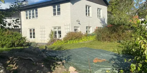 Vitt hus med mörk tak och trädgård. En presenning täcker en del av trädgården, kanske ett gömt hus skatt?