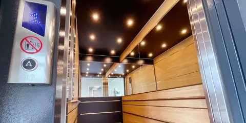 Insidan av en modern, men ändå gammal hiss, med träpaneler, speglade väggar och en svart tak med spotlights. En knapp med siffran 1 lyser.