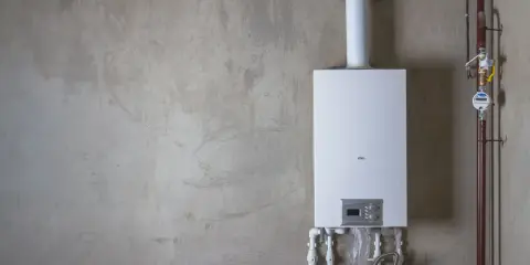 Installation av varmvattenberedare, pris och funktioner. En vit varmvattenberedare monterad på en betongvägg med röranslutningar.