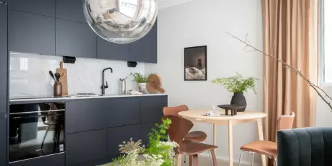 Modernt kök med mörkblå skåp, marmorstänkskydd och ett runt matbord. Perfekt för den som drömmer om ett eget hem med bolån student.