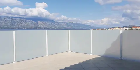 Frosted glass privacy screens on a tiled patio with a view of mountains and the sea.