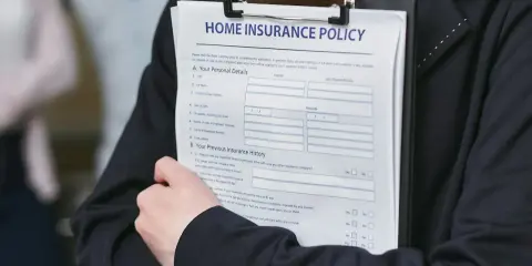 Person håller ett dokument med rubriken "HOME INSURANCE POLICY". Detta kan vara en del av ett hyresavtal lokal.