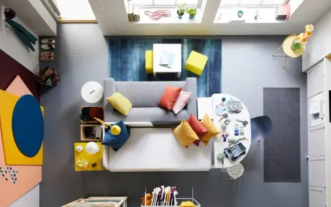 Ett litet vardagsrum med matplats, fyllt med färg och kreativitet. En grå soffa med kuddar i orange och gult, en vit matplats med stolar och en blå matta.