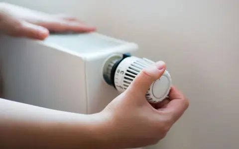 En hand vrider på termostaten till ett vattenburet element för att justera värmen.