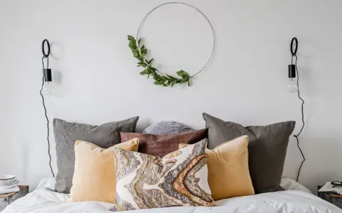 Sovrum inspiration med en säng fylld av kuddar i olika färger och texturer, en grön krans på väggen och minimalistiska vägglampor.