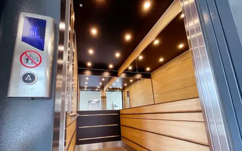 Insidan av en modern, men ändå gammal hiss, med träpaneler, speglade väggar och en svart tak med spotlights. En knapp med siffran 1 lyser.