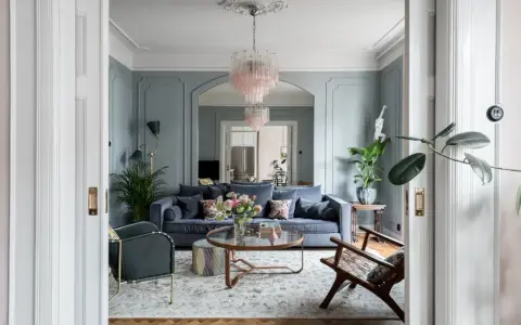 Ett elegant vardagsrum med blåa väggar, en mörkblå soffa, en rosa kristallkrona och en vacker matta. Perfekt vardagsrum inspiration för ett stilfullt hem.