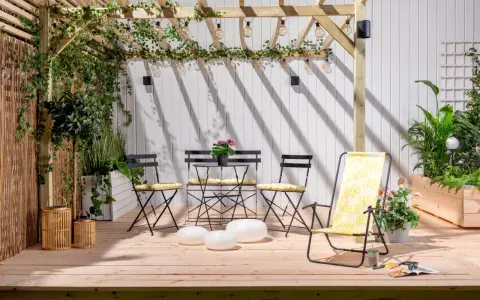 En mysig uteplats med träpergola, belysning och sittgrupp. Buskar insynsskydd ger avskildhet.