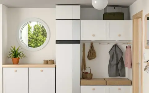 Hall med vit inredning, en NIBE F735 värmepump, fönster, trappa och klädkrok.