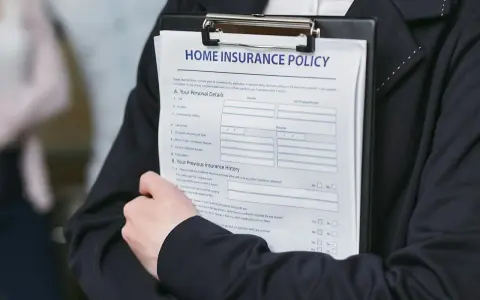 Person håller ett dokument med rubriken "HOME INSURANCE POLICY". Detta kan vara en del av ett hyresavtal lokal.