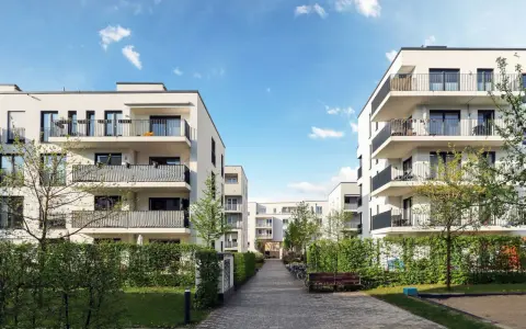 Moderna bostadshus med balkonger och grönska. En lugn innergård med gångväg, bänk och cyklar. Perfekt för en trygg boendemiljö, som en revisor brf skulle uppskatta.