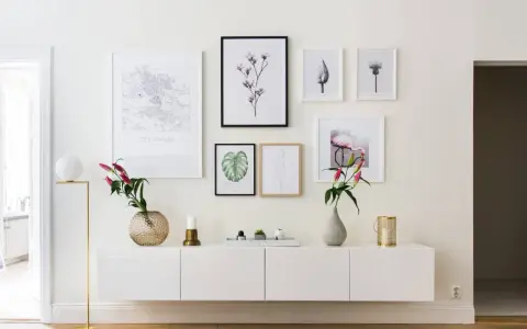 Ett modernt, inrett avlastningsbord med konstverk och blommor. En vit skänk med en guldig lampa, vaser och ljus.