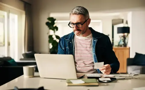 Man med glasögon kollar papper och laptop, kanske för att se vad kollar banken vid bolån.